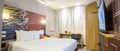 A hotel room with a large bed, a desk with a chair, a television, and a wall-mounted TV.