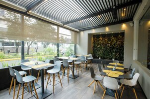 Un restaurante moderno con terraza, ventanas amplias y una pared verde con plantas.