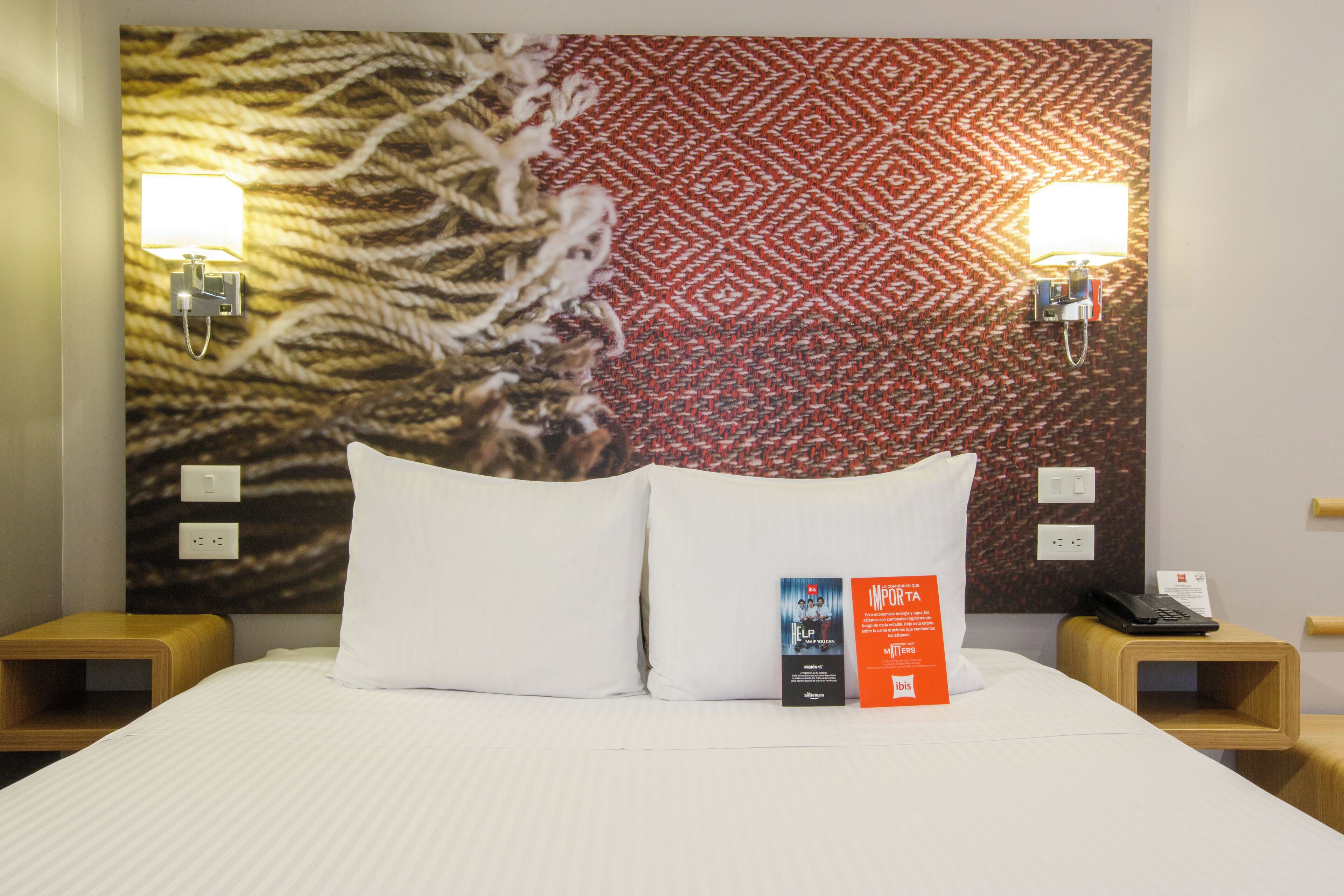 A hotel room with a bed, two bedside tables, a wall with a patterned design, and two wall-mounted lamps.