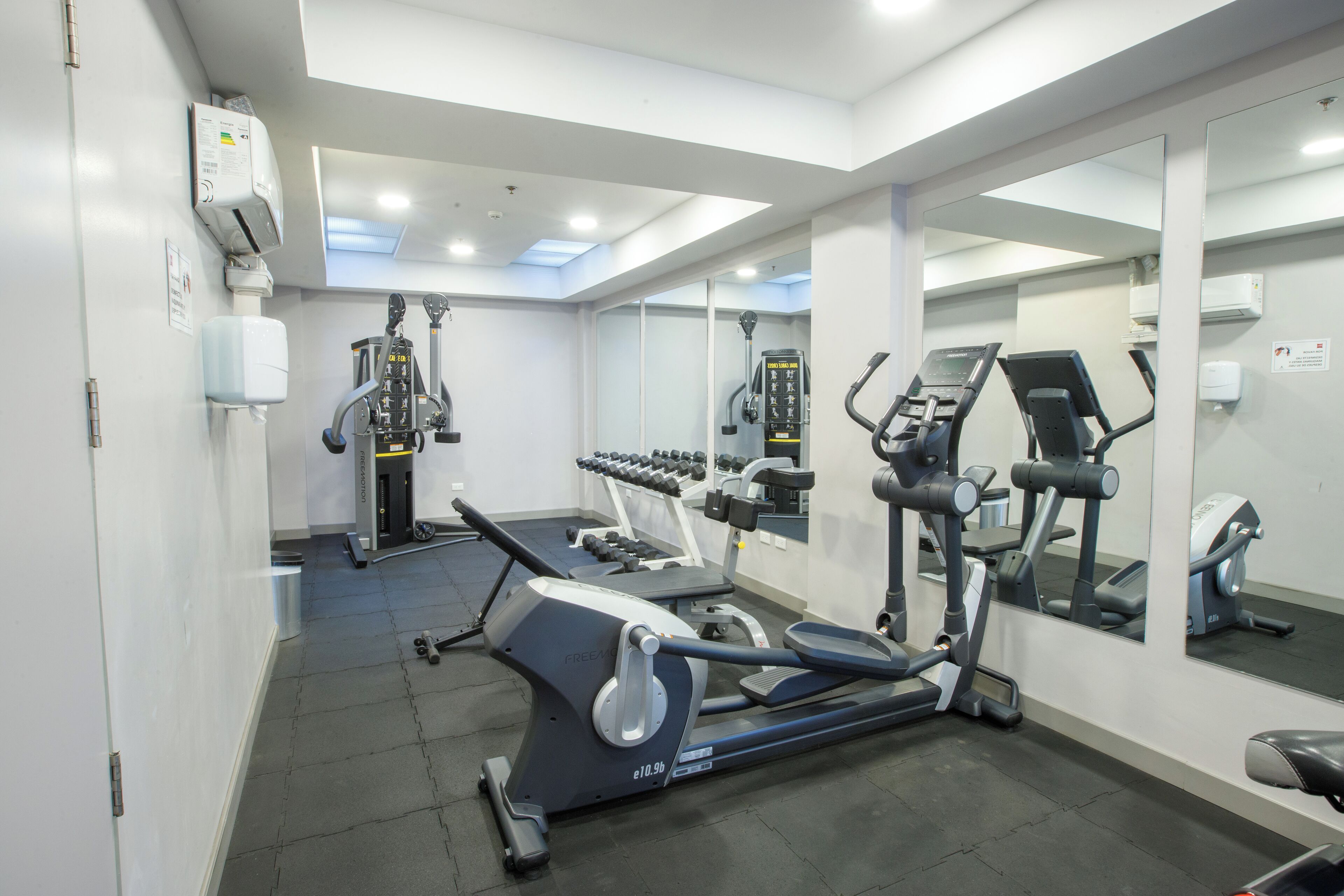 Un gimnasio moderno con máquinas de cardio, pesas libres y espejos.