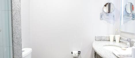 Un baño con inodoro blanco, lavamanos con espejo, toallero y zona de ducha.