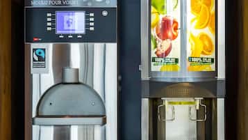 Due macchine da caffè con interfacce digitali e manifesti a tema frutta.