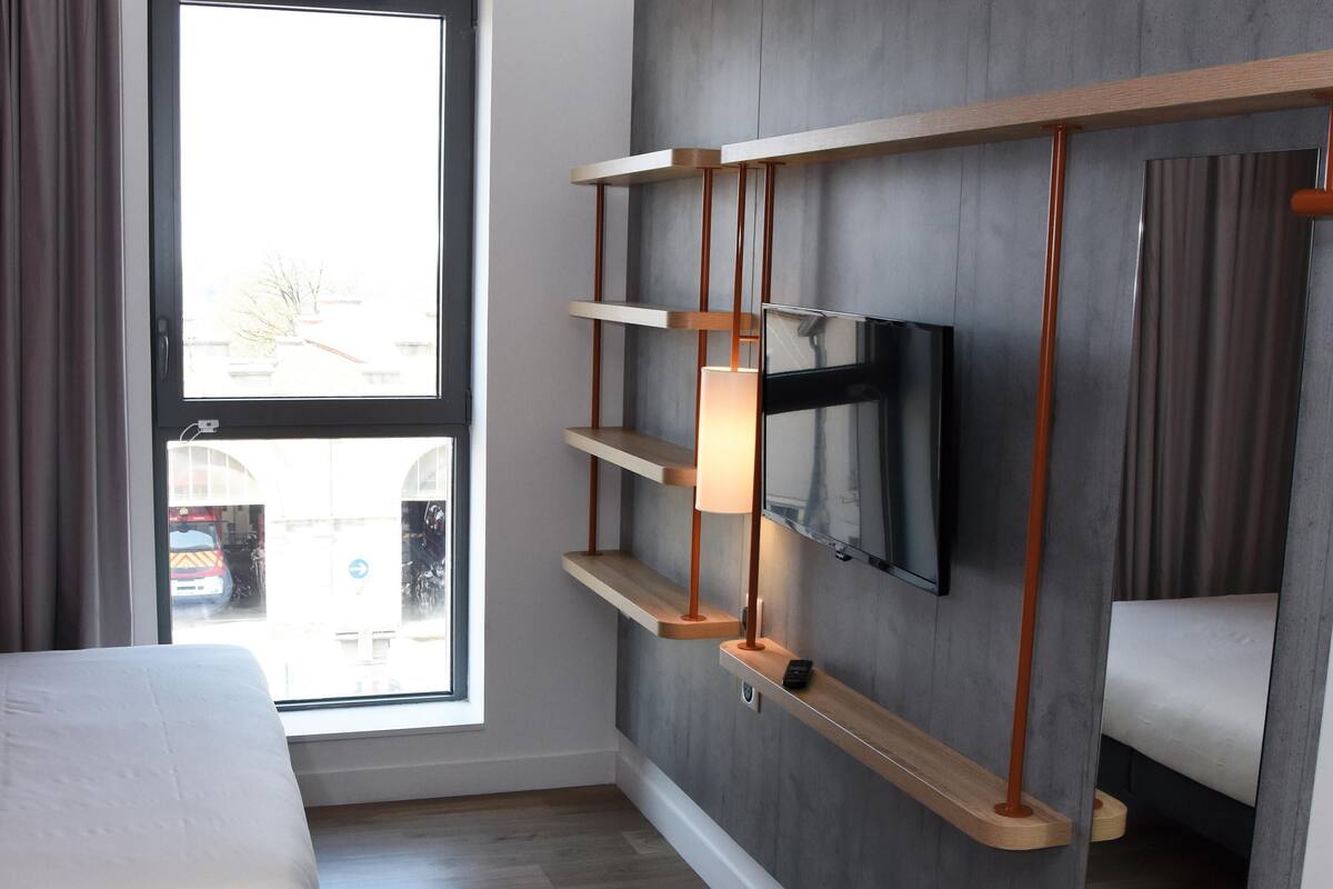 Een hotelkamer met een bed, een aan de muur bevestigde televisie en een raam met uitzicht.
