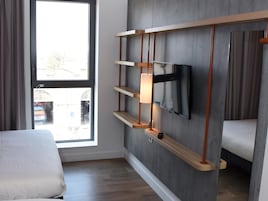Habitación de hotel con cama, televisor montado en la pared y ventana con vistas al exterior.