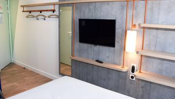 A modern hotel room with a mounted TV, wooden shelves, and a bedside table.