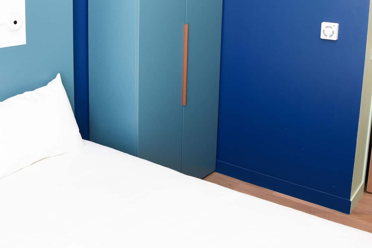 Een slaapkamer met een bed, een blauwe garderobe en een witte stopcontact.