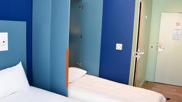 A hotel room with two beds, a wardrobe, a door with a sign, and a light switch on the wall.