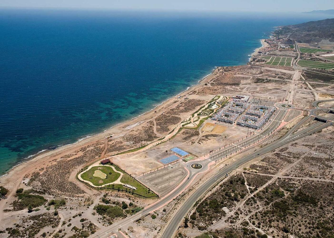 An aerial view of a coastal development with a marina, roads, and green spaces.