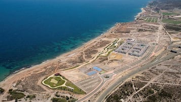 An aerial view of a coastal development with a marina, roads, and green spaces.