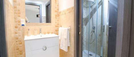 Un baño moderno con ducha envuelta en vidrio, tocador blanco con espejo y paredes de baldosas color beige.