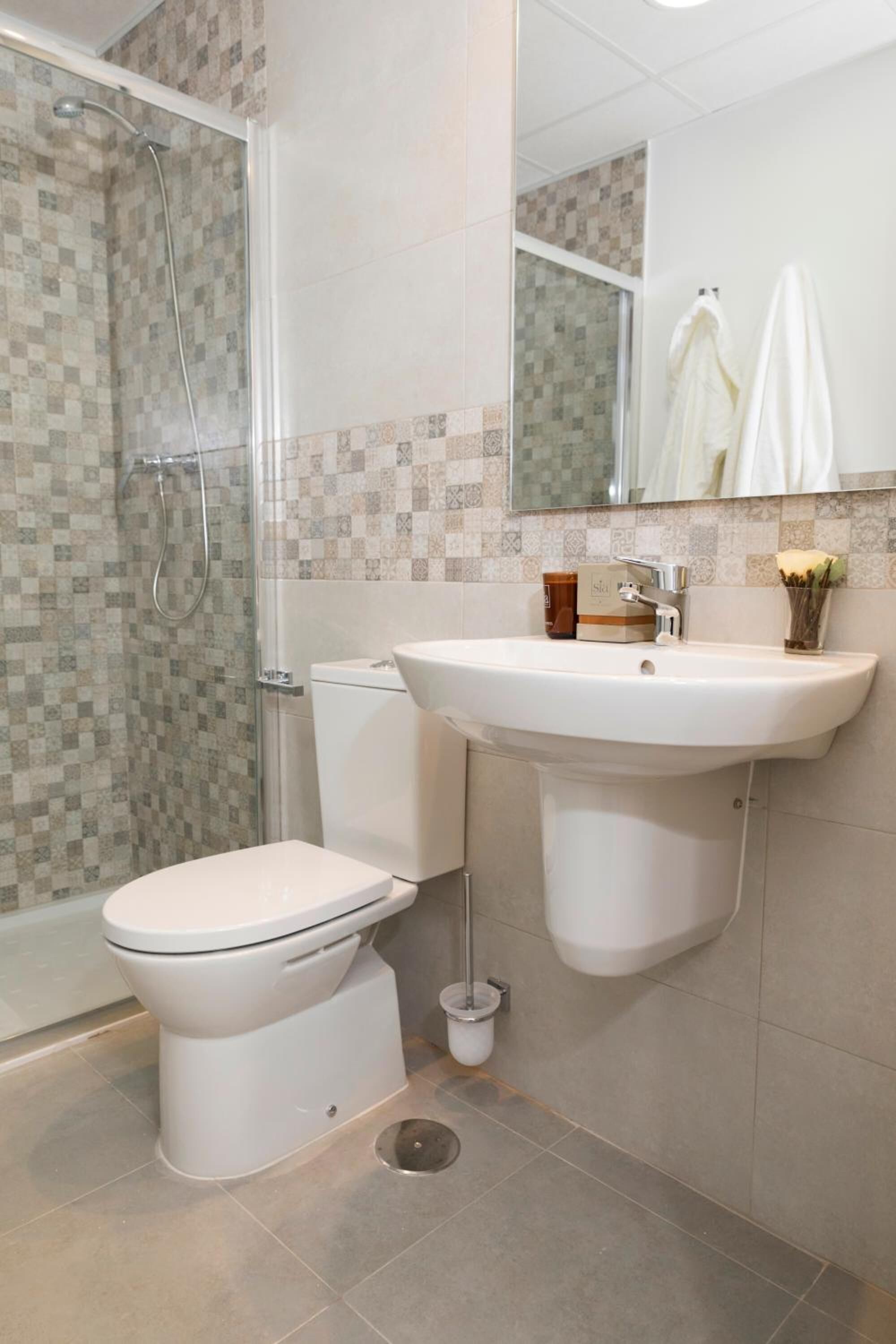 Baño con ducha, inodoro, lavabo y espejo.