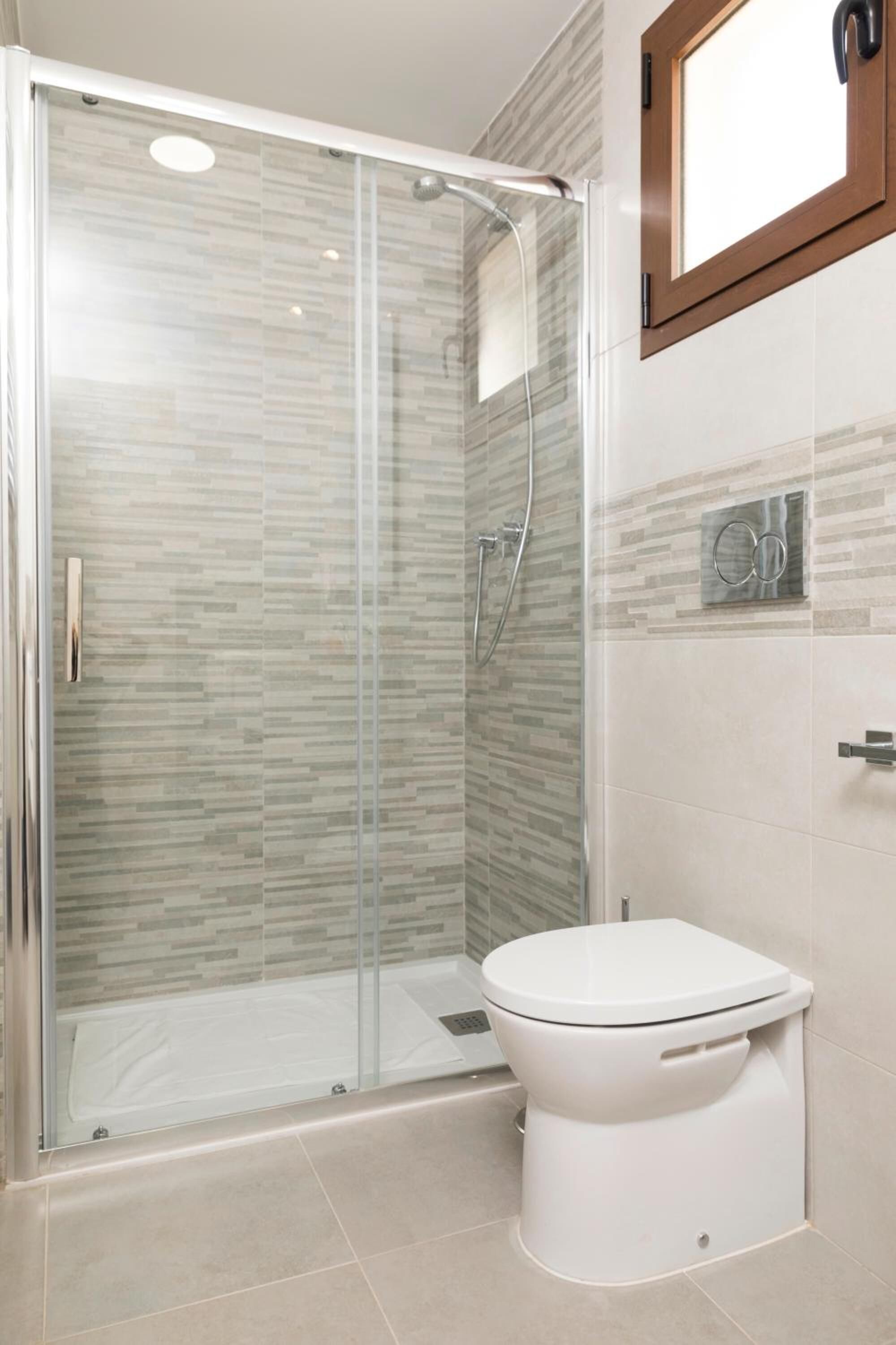 Een moderne badkamer met een glazen douchecabine, toilet en een wandwastafel.