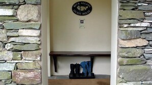 A stone wall with a sign reading "Beck Allans Guest House" and a coat rack with boots and a jacket. - Beck Allans Guesthouse (Ambleside)