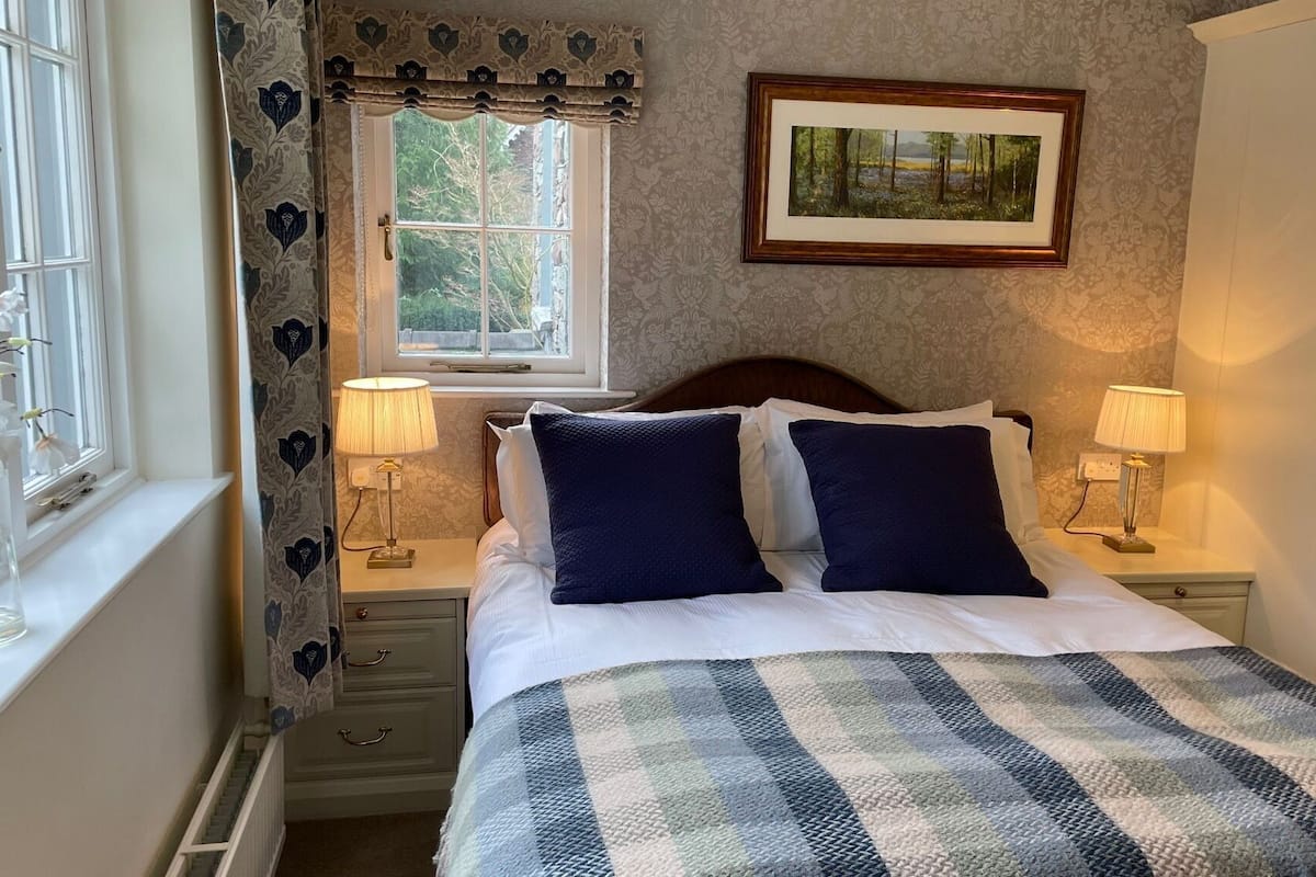 A neatly made bed with two pillows, a checkered blanket, and two bedside lamps.