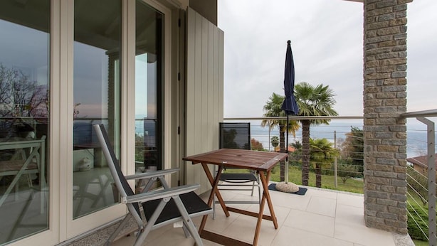 A balcony with a table and chairs, a view of the sea, and a stone pillar. - Contemporary 3 Bed Italian Lakes Villa, Lake Views, Wifi, BBQ (Massino Visconti)
