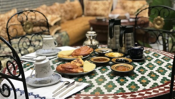 A dining table with a Moroccan-style tablecloth, surrounded by metal chairs. - Riad Salma (Fes)