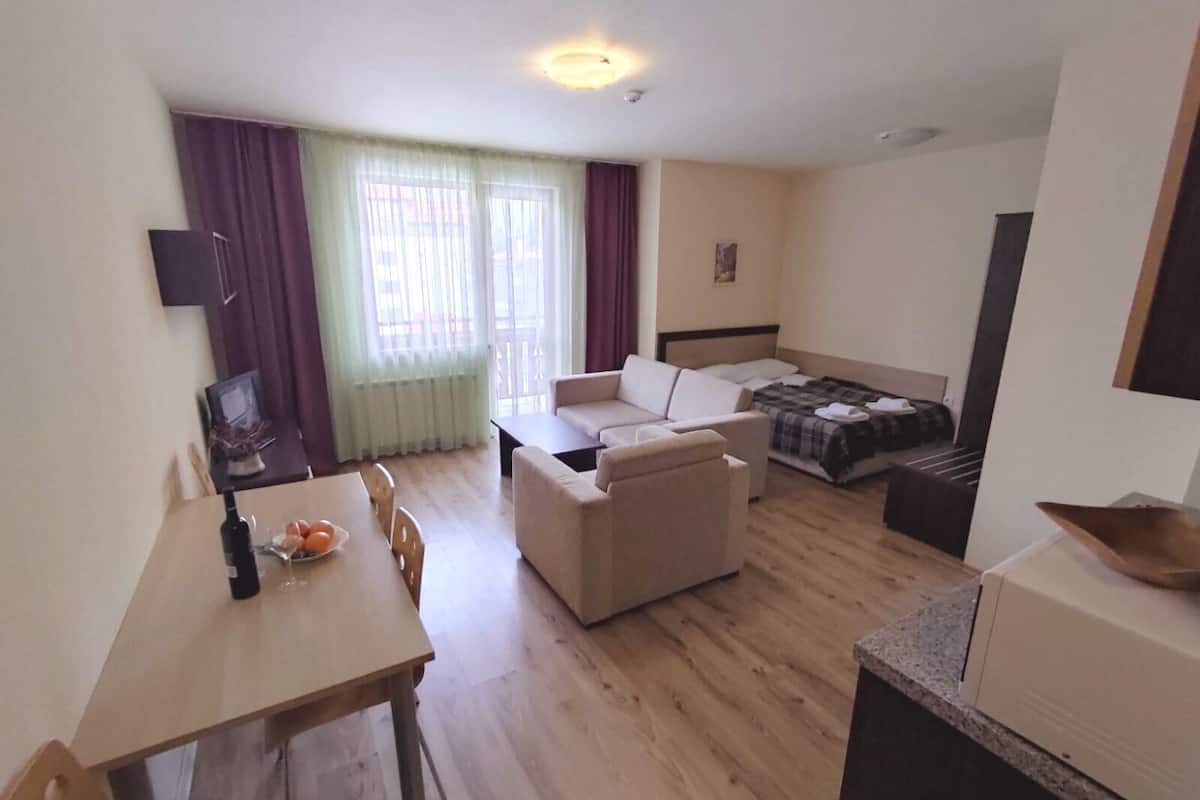 A compact hotel room with a dining area, a sofa, a bed, and a small kitchenette.