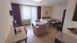 A compact hotel room with a dining area, a sofa, a bed, and a small kitchenette.
