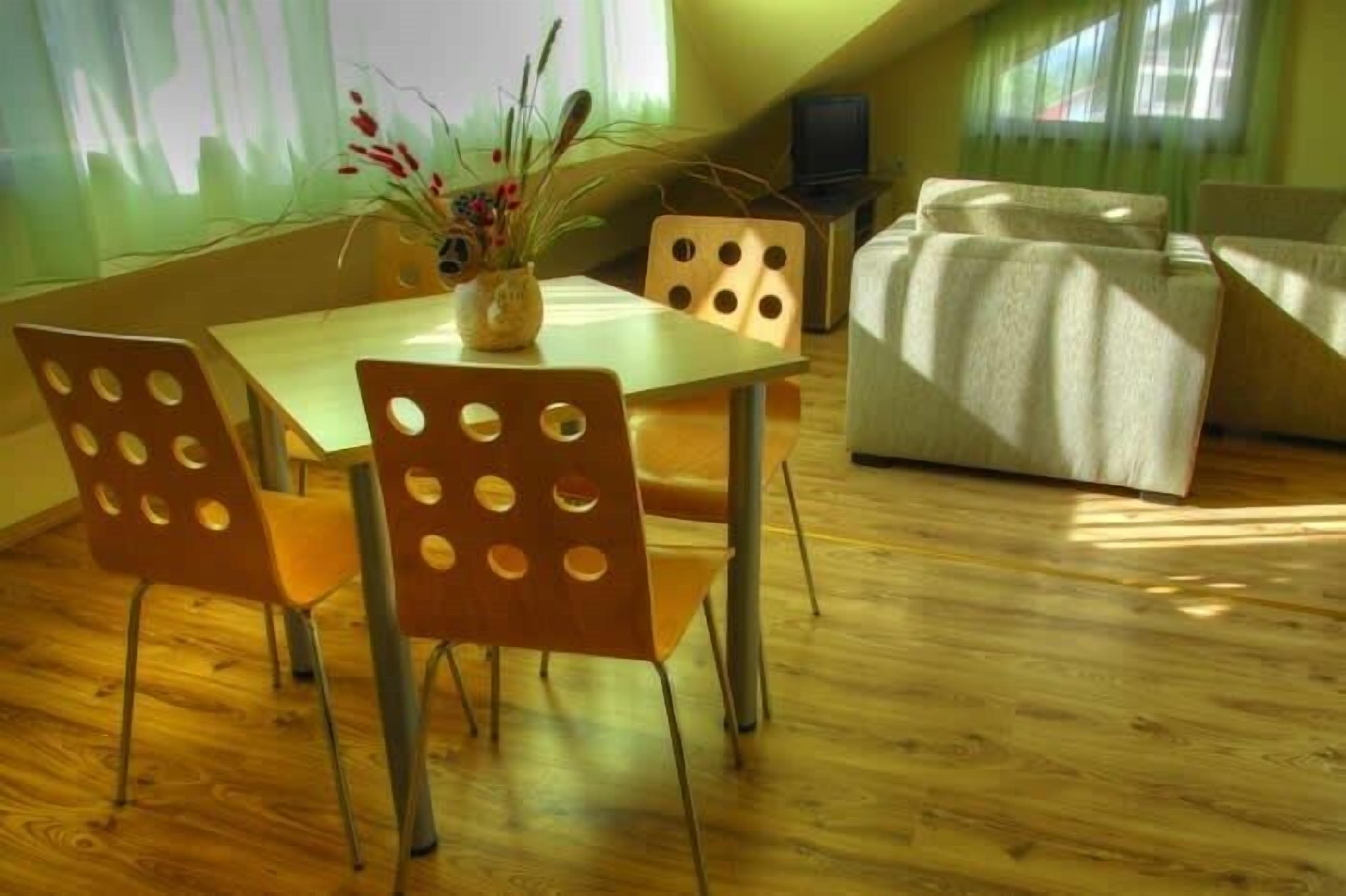 Ein Essbereich mit einem Holztisch und Stühlen, einer Vase mit Blumen und einer Couch im Hintergrund.