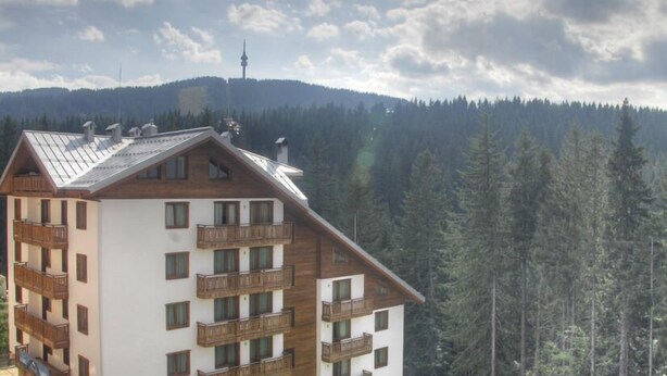 Un hôtel à plusieurs étages, doté de balcons, situé au pied d’une montagne boisée.