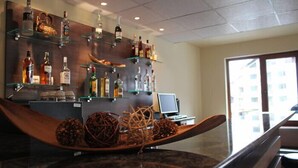 Un coin bar avec des étagères remplies de bouteilles d’alcool, un bol en bois contenant des objets décoratifs et un écran d’ordinateur posé sur un bureau.