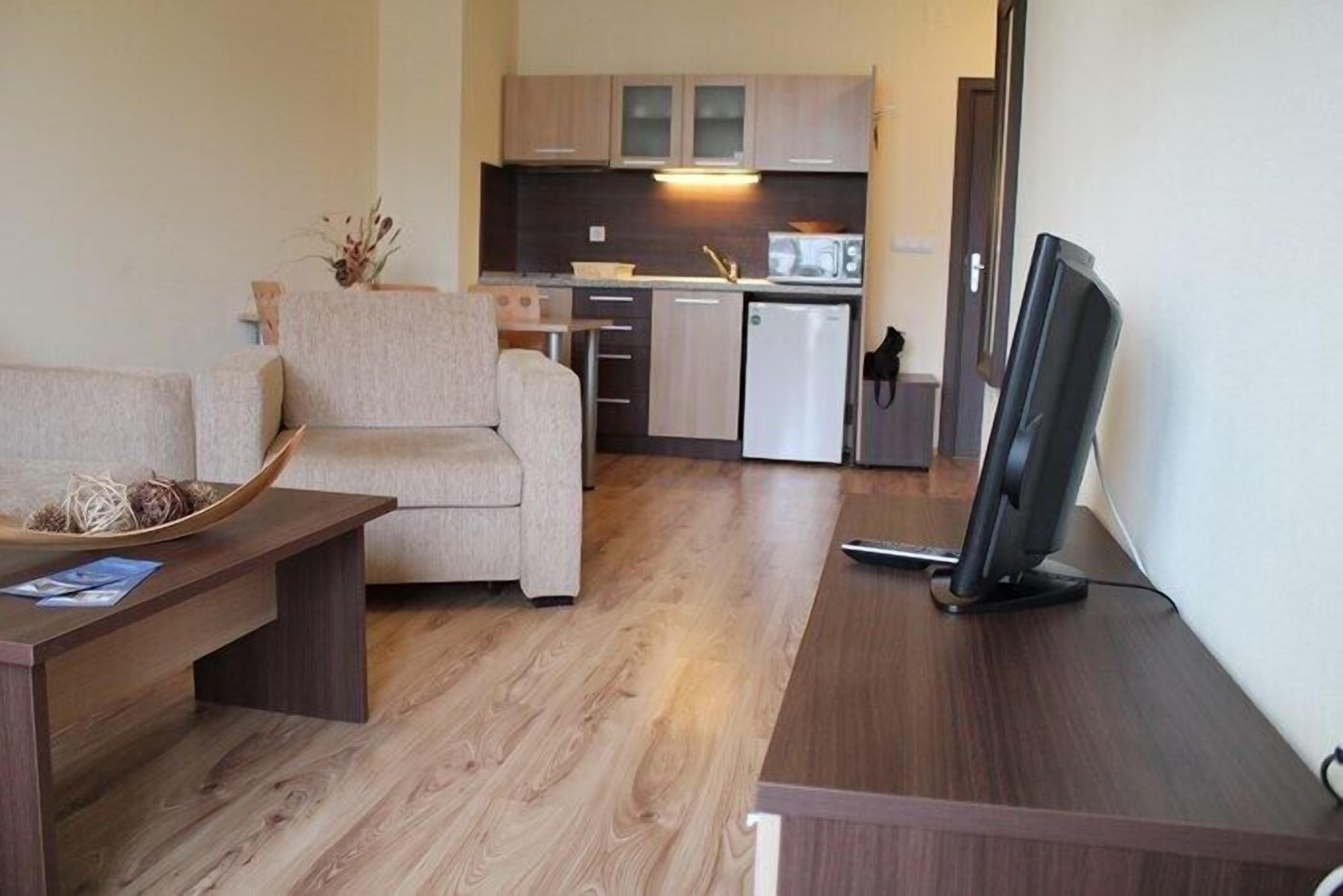 Un espacio habitable compacto con sofá, una mesita de centro, televisor de pantalla plana, kitchenette con microondas, refrigerador y piso de madera.