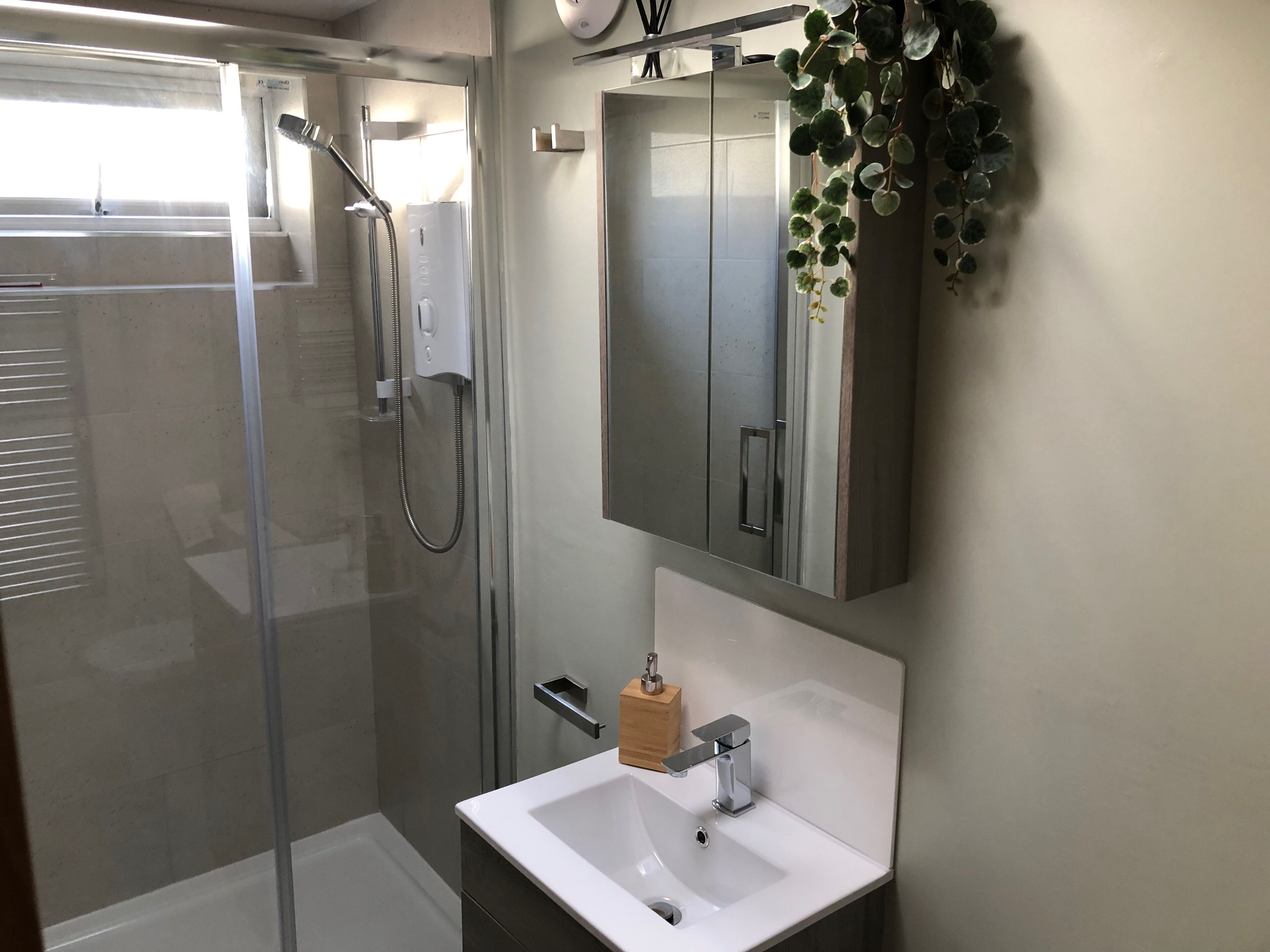 Un bagno moderno con cabina doccia in vetro, lavandino bianco e dispenser per sapone in legno.