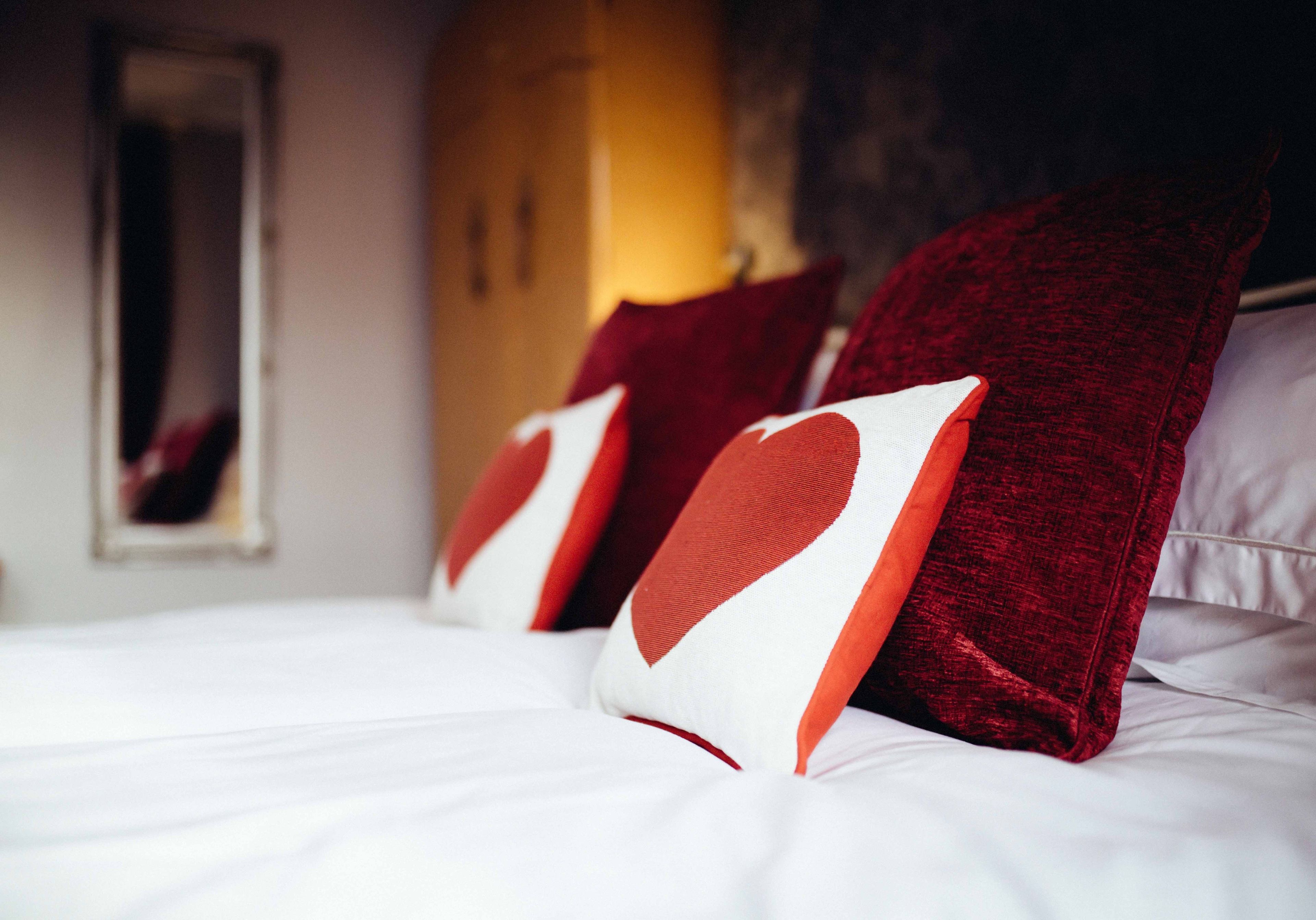 A bed with white bedding and red pillows with heart designs.