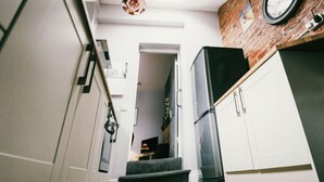 A narrow hallway with a staircase leading to a landing, a refrigerator, and a clock on the wall. - Coalminer's Cottage (Gateshead)