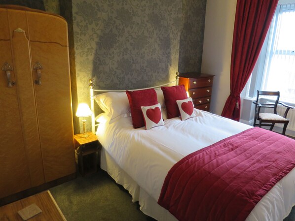 A hotel room with a large bed, a wardrobe, a nightstand with a lamp, a chair, and a window with curtains. - Coalminer's Cottage (Gateshead)