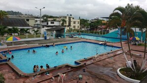 En swimmingpool med flere baner, omgivet af palmer og nogle bygninger i baggrunden.