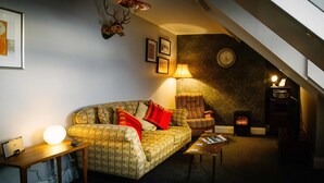 Un salon chaleureux avec un canapé à motifs, une table basse en bois, une lampe, une horloge au mur et une cheminée.