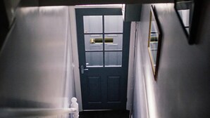 Un escalier menant à une porte dotée d’une fenêtre, d’une sonnette et d’un petit objet blanc fixé au mur.