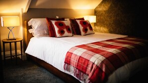 Un lit bien fait, recouvert d’une couverture à carreaux rouges et blancs, avec deux lampes de chevet et des coussins à motifs floraux.