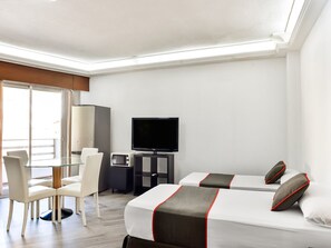 A hotel room with two beds, a desk with a computer, a TV, and a seating area with chairs. - Hello Feria (Madrid)