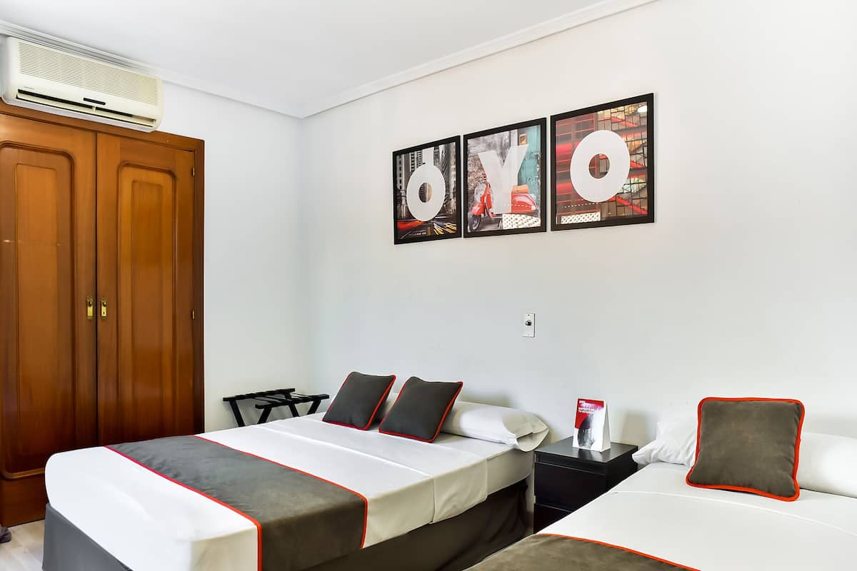 Habitación de hotel con dos camas, un armario, un escritorio y una pared decorada con tres cuadros.