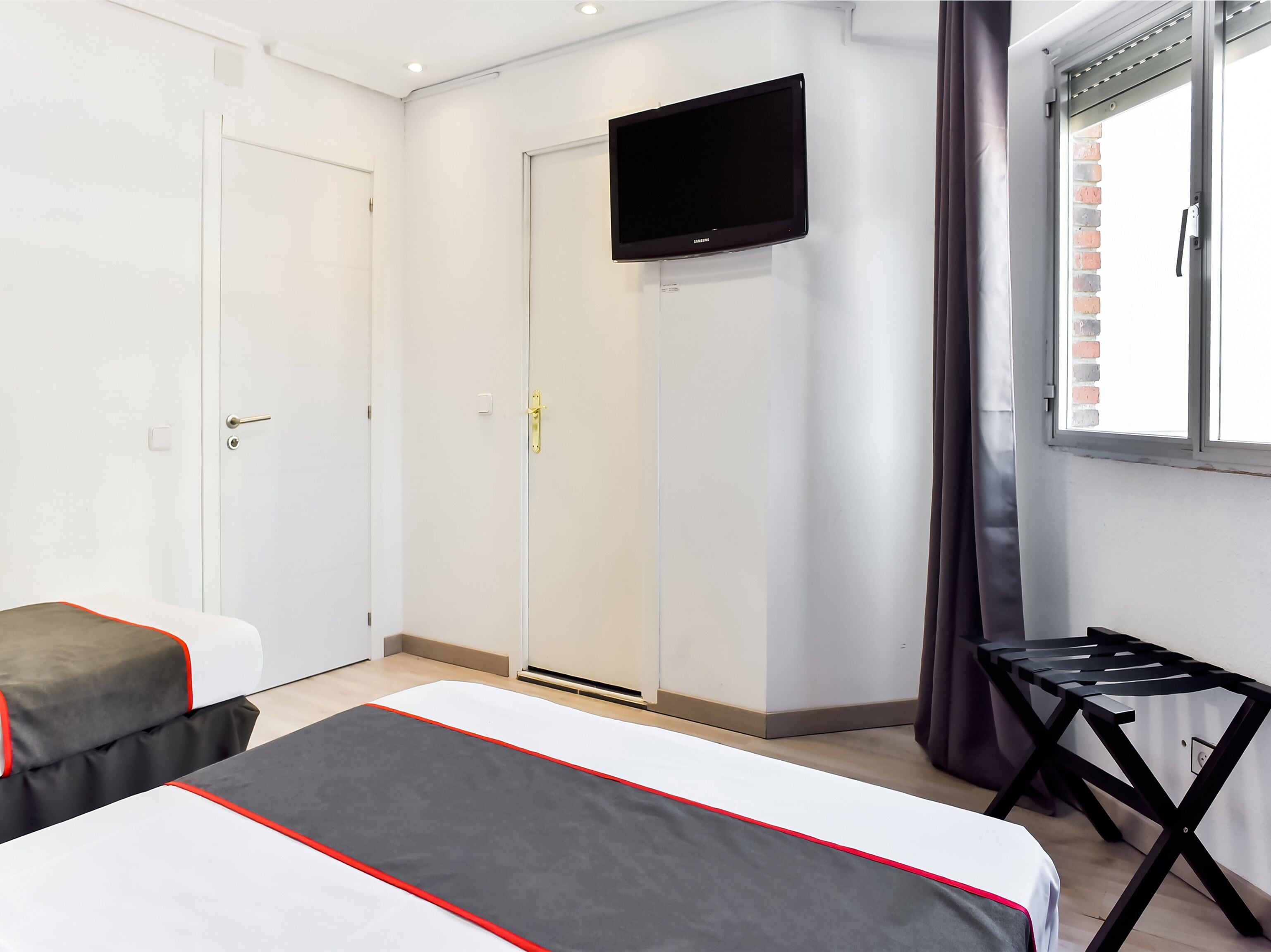 A hotel room with two beds, a TV mounted on the wall, and a window with curtains.