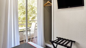 Una habitación con televisión montada en la pared, una banca, una silla y un balcón con mesa y sillas.