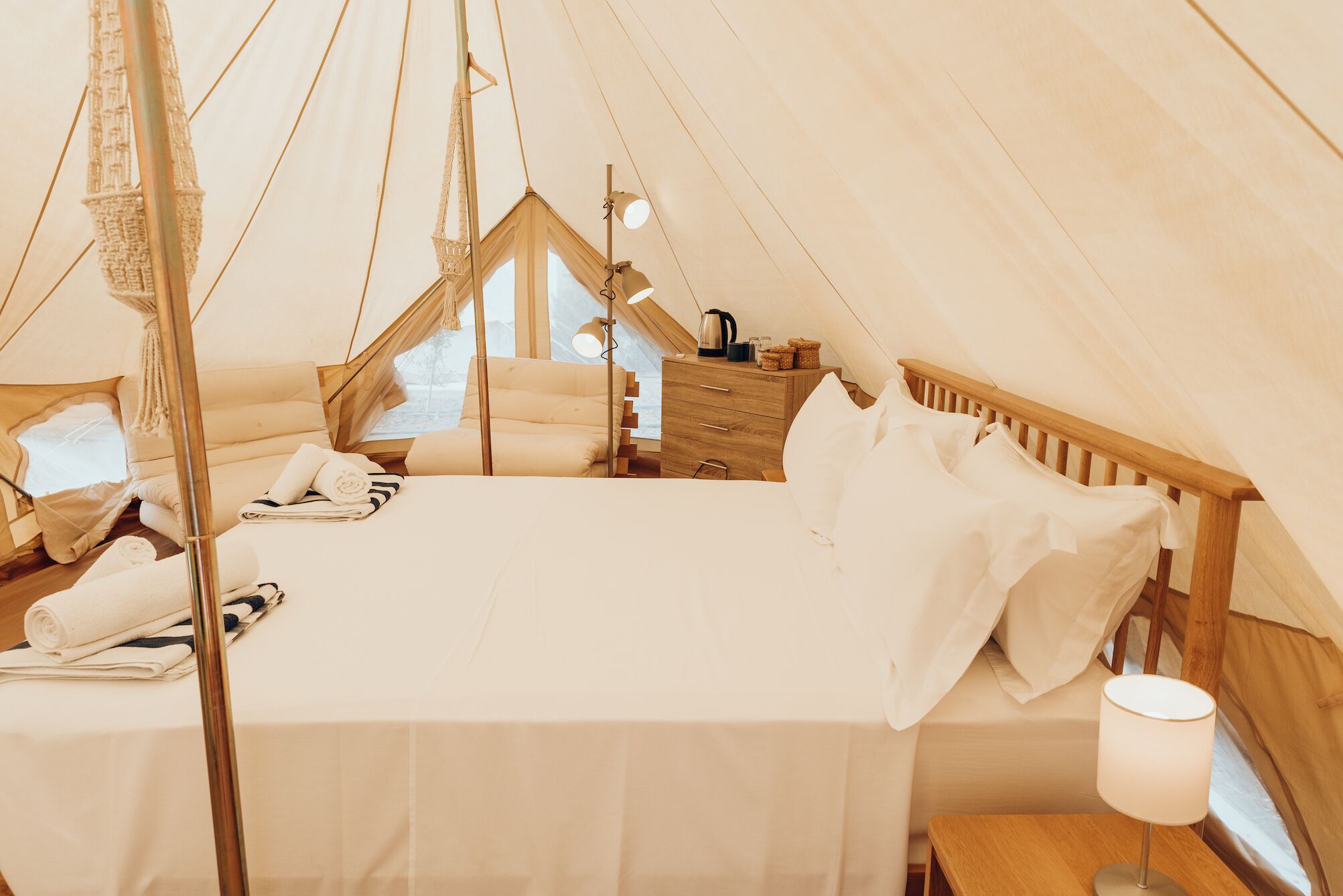 A cozy tented accommodation with a bed, pillows, a bedside table, a lamp, and a window.