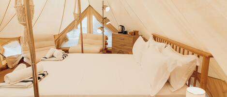 A cozy tented accommodation with a bed, pillows, a bedside table, a lamp, and a window.