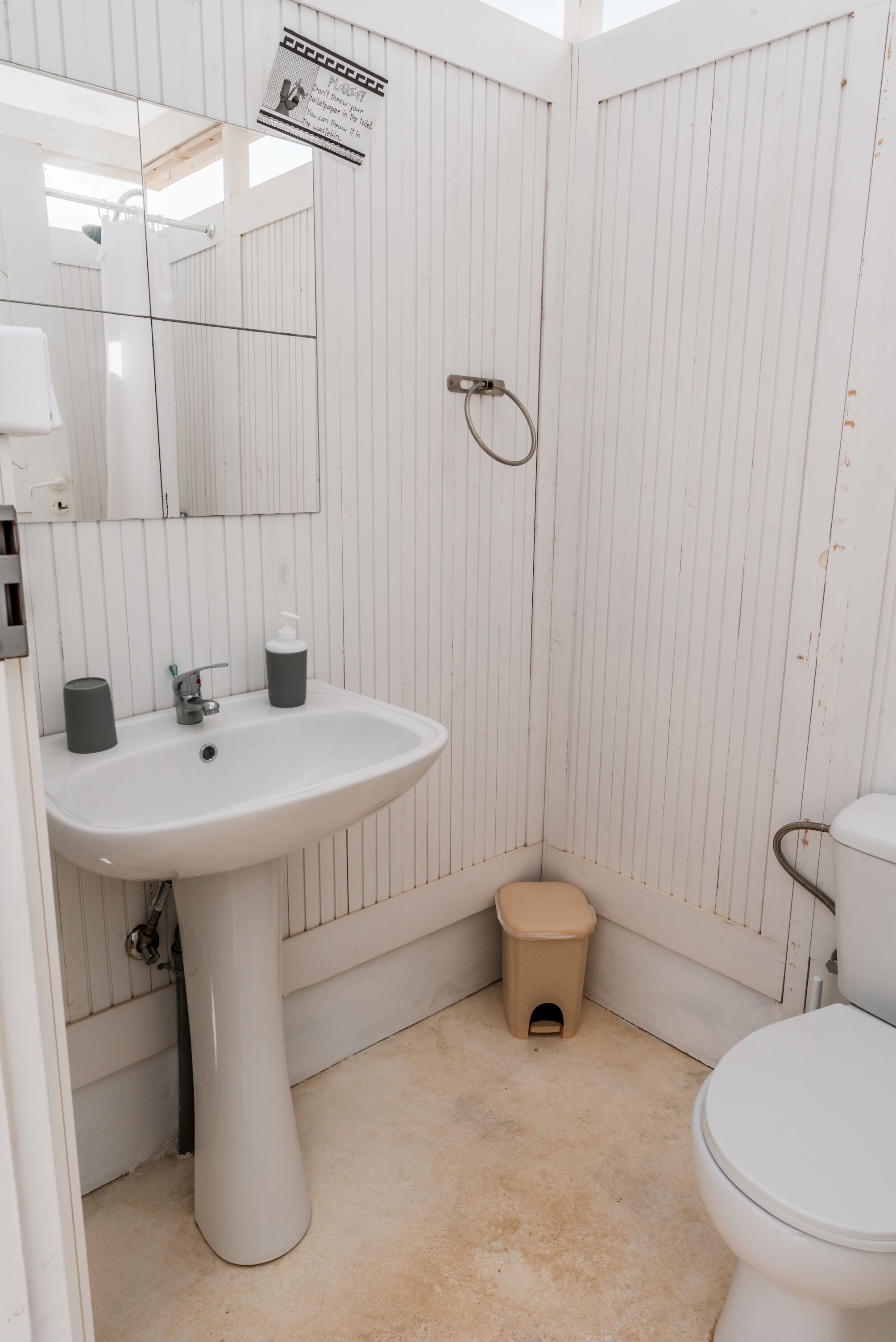 Une salle de bain avec un lavabo blanc, un miroir, des toilettes et une petite poubelle.