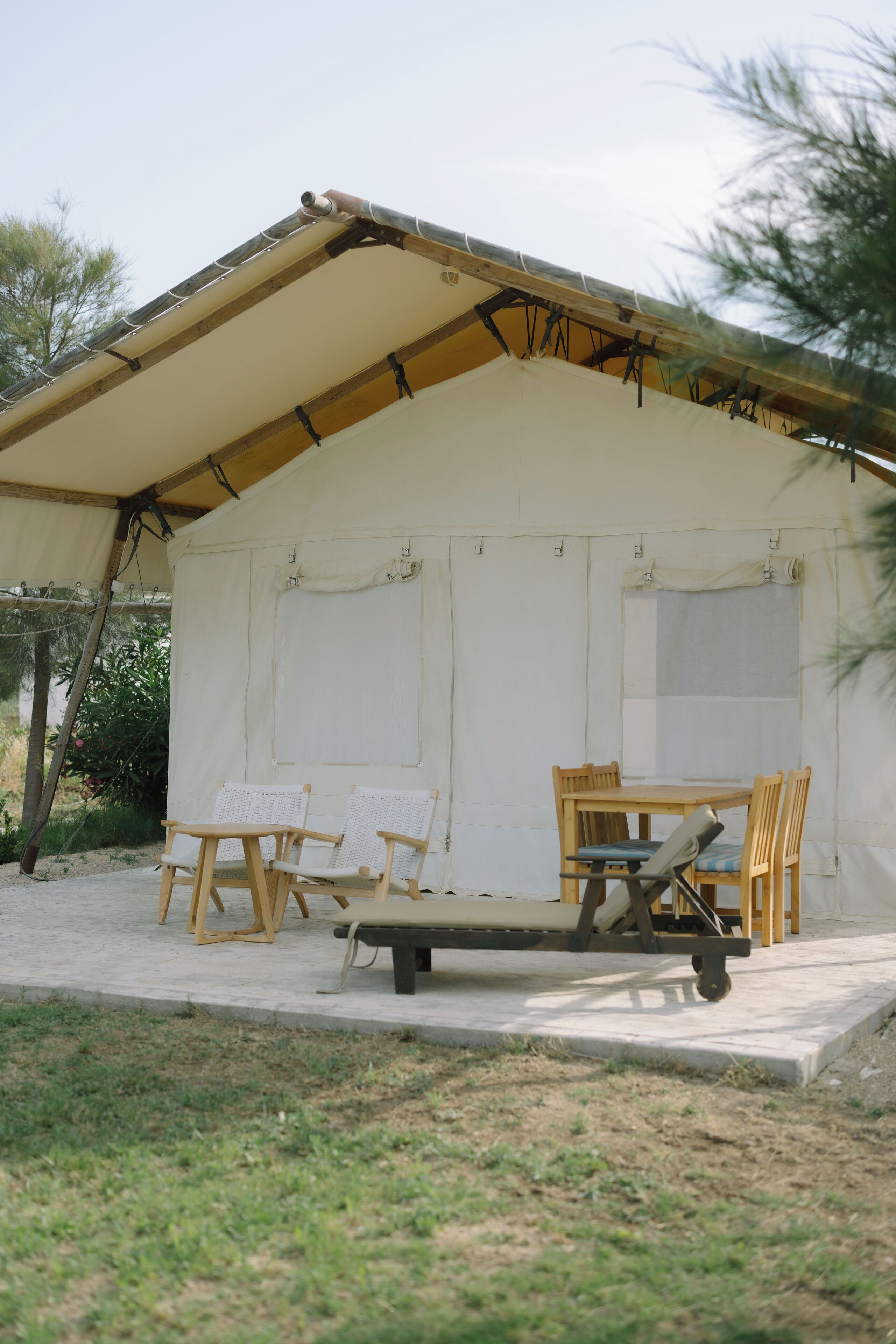 A tented structure with a dining table and chairs, a bench, and a small table with a chair.