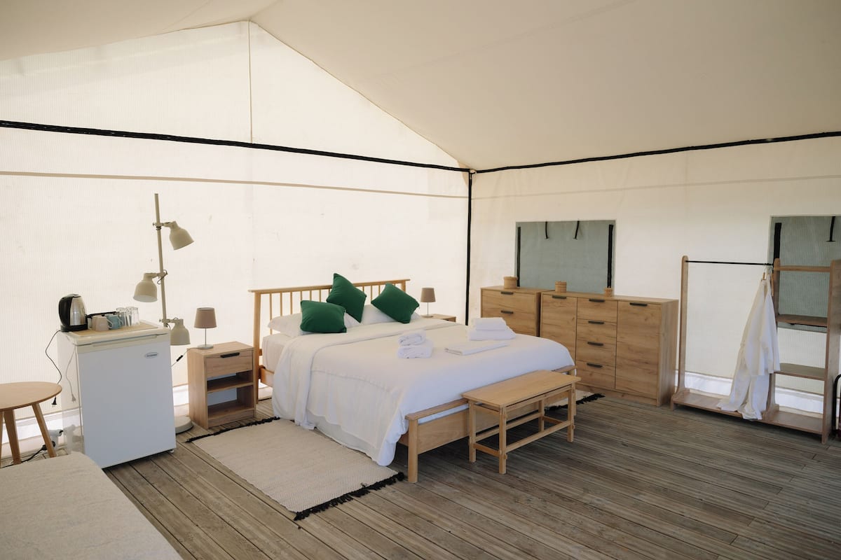 Habitación con tienda de campaña, una cama, muebles de madera, un escritorio y un refrigerador pequeño.