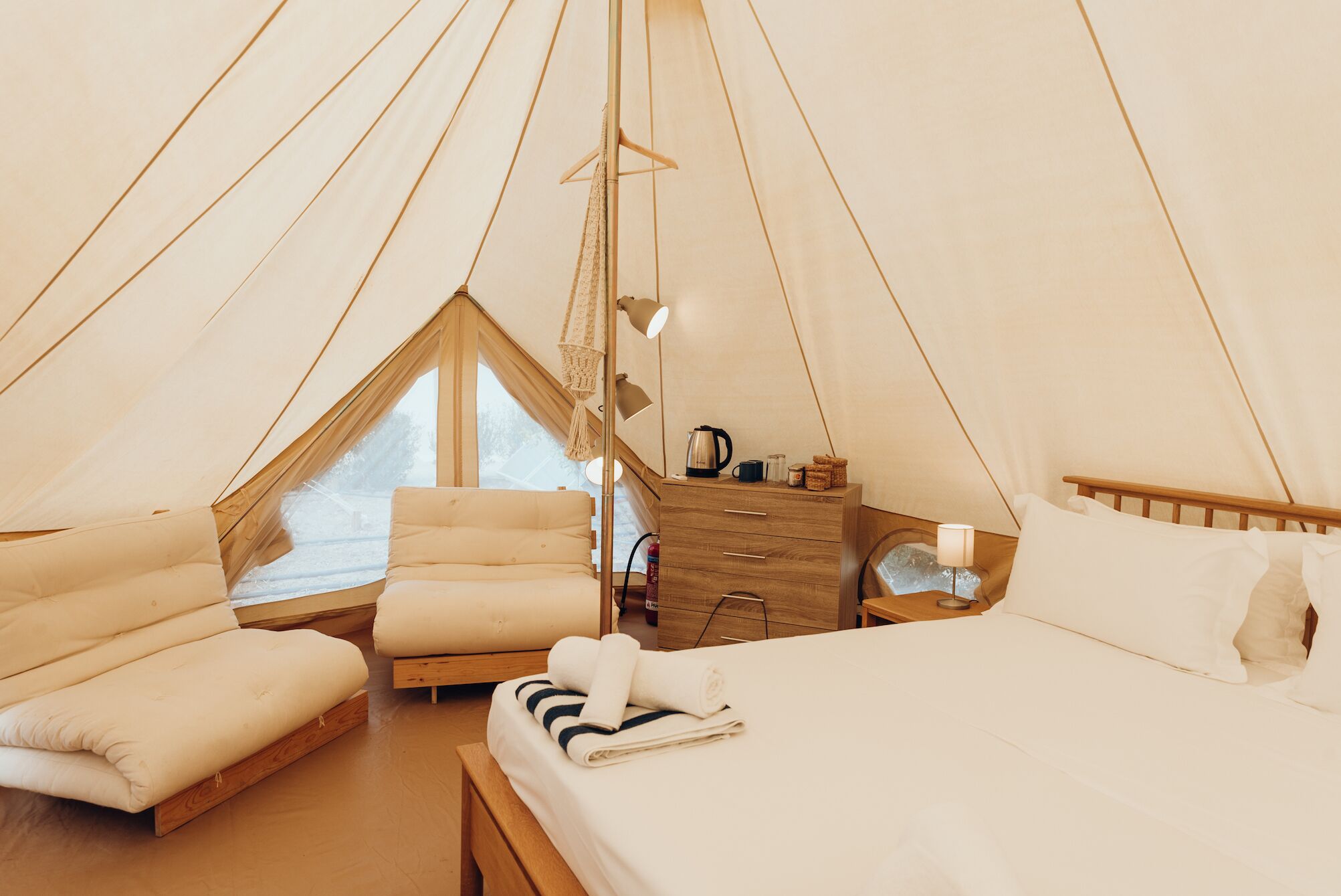 Un dormitorio tipo tienda de campaña acogedor, con una cama, una silla, un aparador de madera y una ventana.