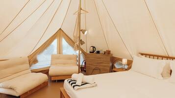 Un dormitorio tipo tienda de campaña acogedor, con una cama, una silla, un aparador de madera y una ventana.