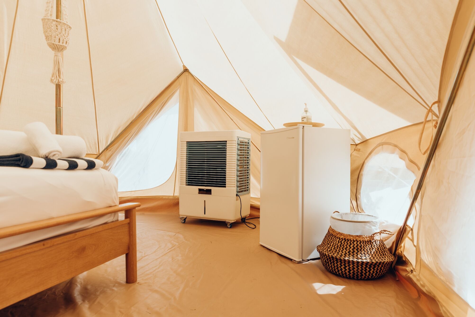 Un accogliente alloggio in tenda, completo di letto, condizionatore portatile, frigorifero e cesto di vimini.