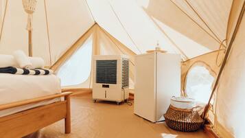 Un accogliente alloggio in tenda, completo di letto, condizionatore portatile, frigorifero e cesto di vimini.