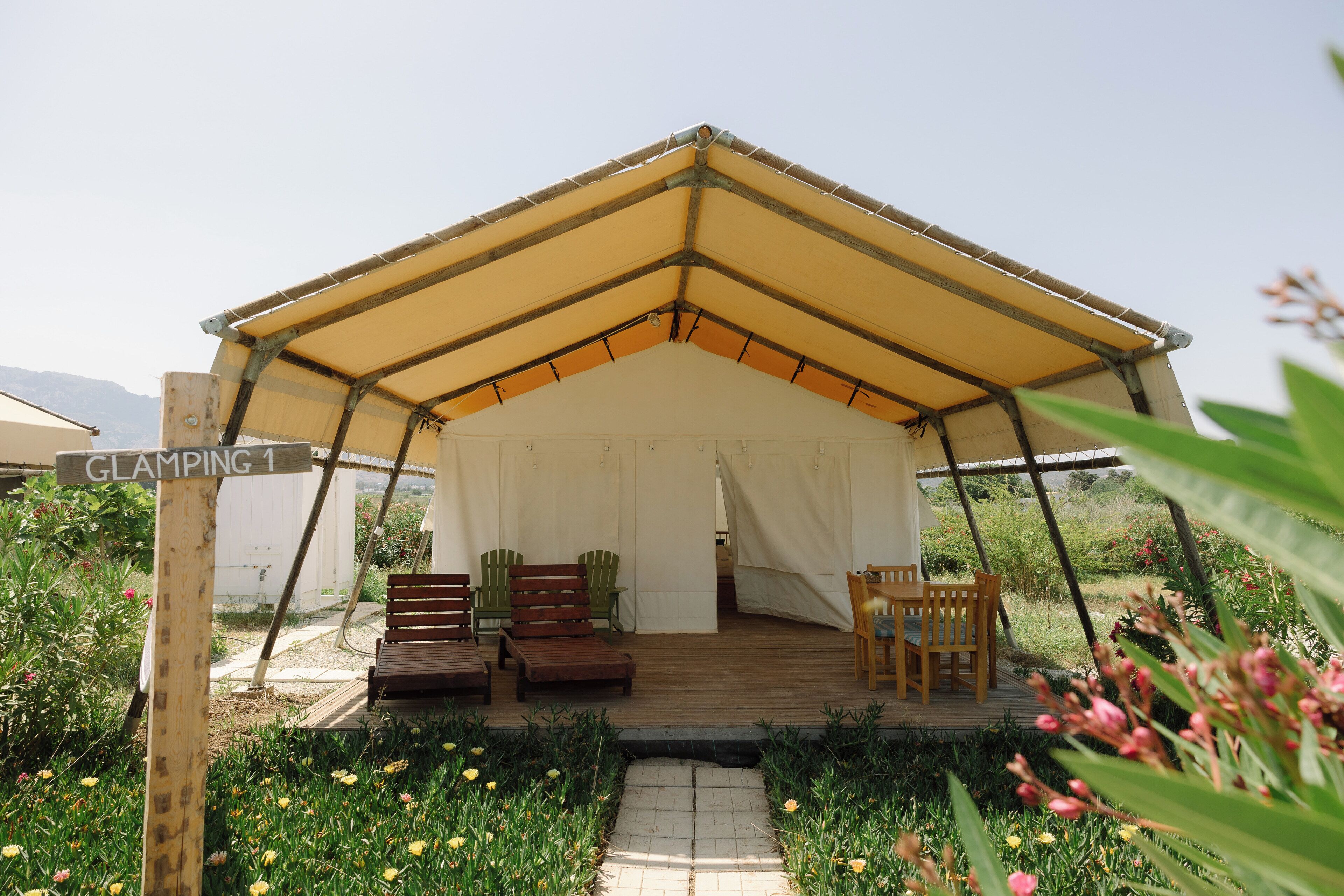 A tented structure with a wooden deck, seating area, and a sign indicating "GLAMPING 1".
