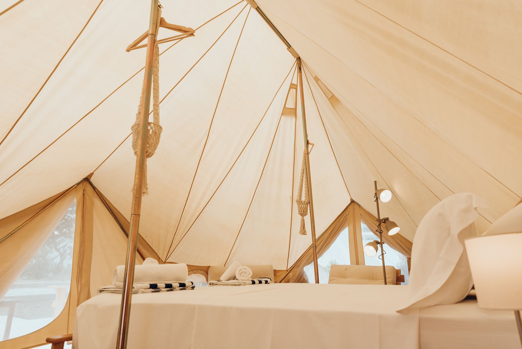 A tent with a bed, pillows, and a hanging light fixture.