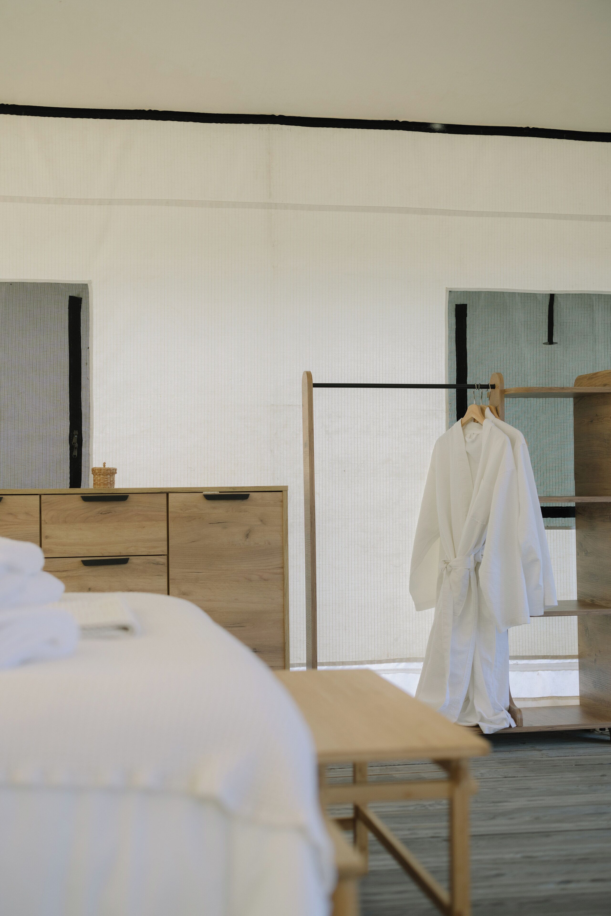 Habitación de hotel con tocador de madera, cama con ropa blanca y bata colgada en un perchero de madera.